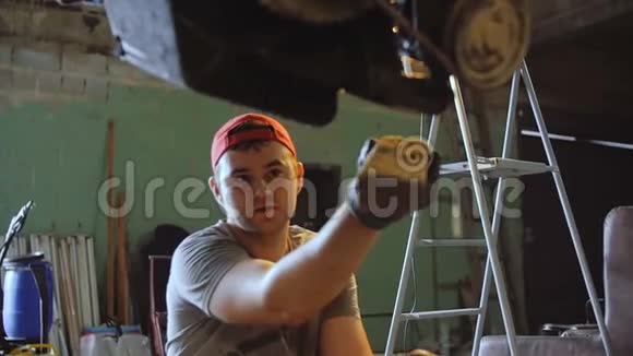 车库里的一名汽车修理工在悬挂的汽车发动机上敲一根木条视频的预览图
