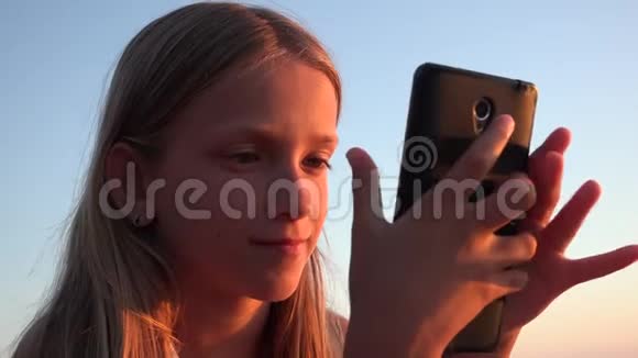儿童玩智能手机孩子在日落海滩女孩在海滨使用平板电脑视频的预览图