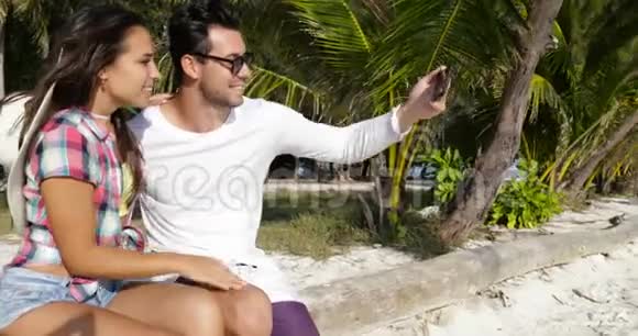 情侣在棕榈树下的手机户外自拍快乐的微笑男人和女人看照片视频的预览图