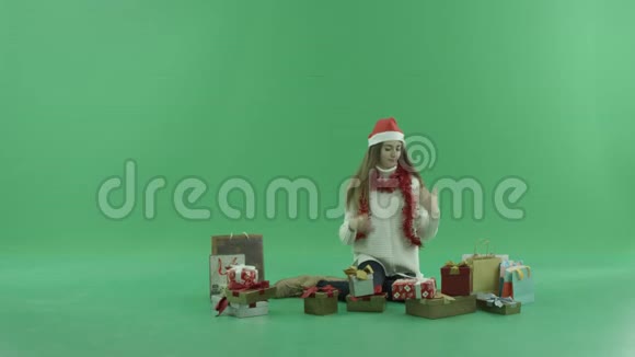 年轻的美女戴着圣诞帽看着她的圣诞礼物和购物袋还戴着彩色钥匙视频的预览图