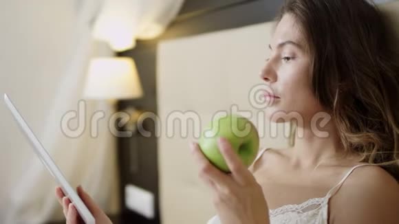 女人在平板电脑上看电影躺在床上闻苹果视频的预览图