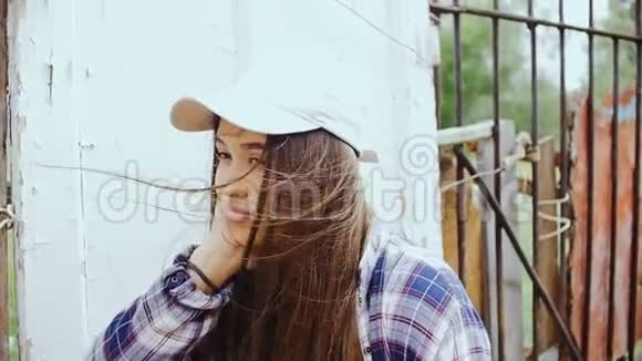一位留着长发和棒球帽的年轻女子站在旧篱笆旁视频的预览图