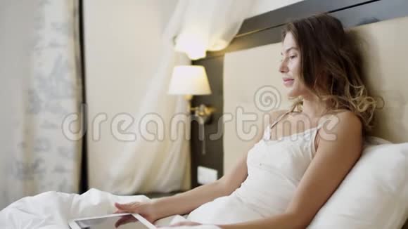快乐的女人躺在床上在平板电脑上做视频翻译视频的预览图