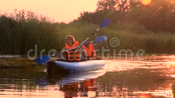 日落时分两个人坐在湖边的皮划艇上划桨慢动作视频的预览图