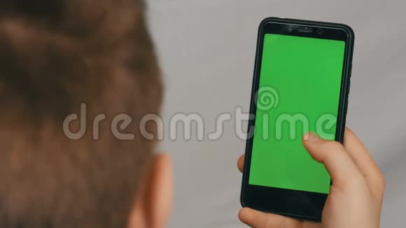 青少年男孩手里拿着一部黑色智能手机白色背景上有一个绿色屏幕技术视频的预览图