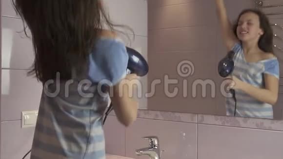 美丽快乐的女孩少年用吹风机吹干头发在浴室的镜子前唱歌跳舞视频的预览图