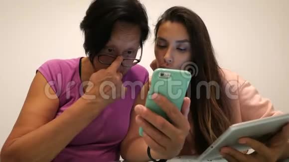 年轻的混血女孩和她的资深亚洲母亲在手机和平板电脑上安装应用程序4k视频的预览图