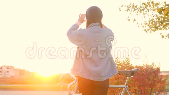 年轻时髦的白种人女孩带着复古自行车用手机拍摄城市日落照片4K慢动作视频的预览图