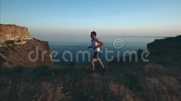 运动帅哥正在用电话和耳机做运动日落时沿着海边跑步然后慢跑视频的预览图