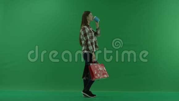 女孩站在她的右边拿着袋子在绿色的屏幕上喝着杯子里的东西视频的预览图