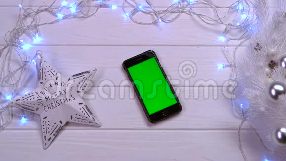 手机躺在白色的桌子上旁边是圣诞玩具和花环顶部视图视频的预览图