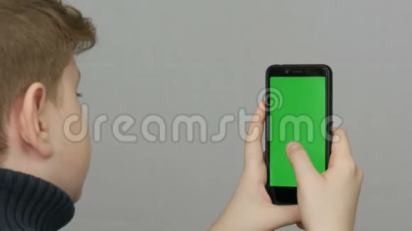 青少年男孩手里拿着一部黑色智能手机白色背景上有一个绿色屏幕技术视频的预览图