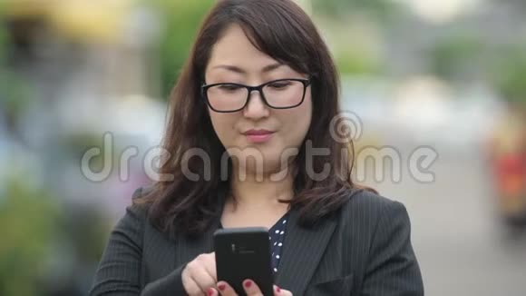 成熟美丽的亚洲女商人在户外的街道上使用电话视频的预览图