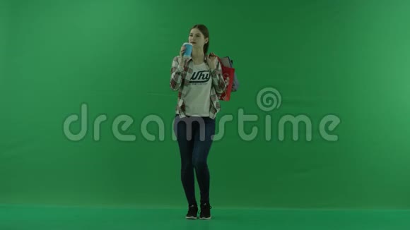 女孩站在那里肩上扛着袋子在绿色的屏幕上喝着杯子里的东西视频的预览图