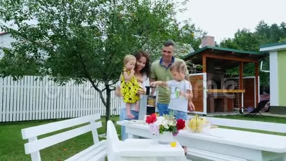 幸福美丽的家庭妈妈爸爸四岁的儿子和一岁的女儿用葡萄做新鲜果汁在夏天视频的预览图