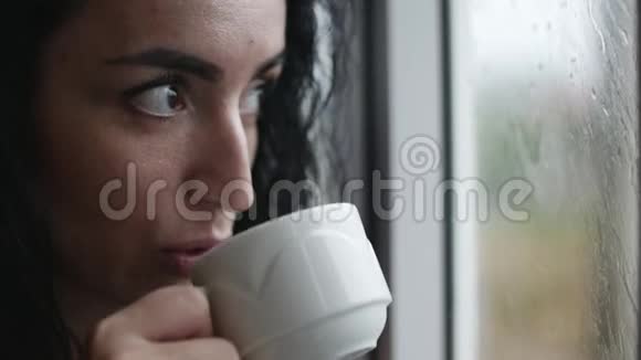 尖酸刻薄的年轻白种人女人看着窗外的雨喝着咖啡视频的预览图