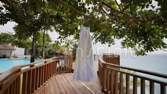 优雅的新娘花边礼服挂在酒店露台上的一棵树上俯瞰大海菲律宾异国风情视频的预览图