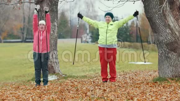 秋公园两位快乐的老年妇女在运动前做热身运动北欧散步视频的预览图