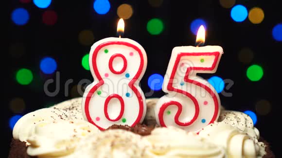 在蛋糕上面的85号八十五岁生日蜡烛燃烧在最后吹灭彩色模糊背景视频的预览图