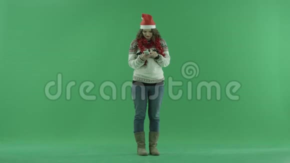 兴奋的年轻女子戴着圣诞帽一边站着一边在智能手机上讲话背景上的彩色钥匙视频的预览图