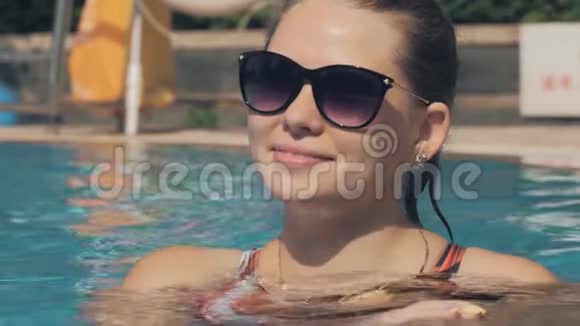 一个美丽的白种人女人的肖像是一个游泳池美丽的长发女孩在蓝色的游泳池里放松视频的预览图