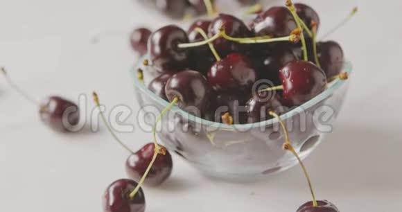 在一张白色桌子上的玻璃碗里用一个成熟的红樱桃做一个全景式的慢动作特写背景模糊视频的预览图