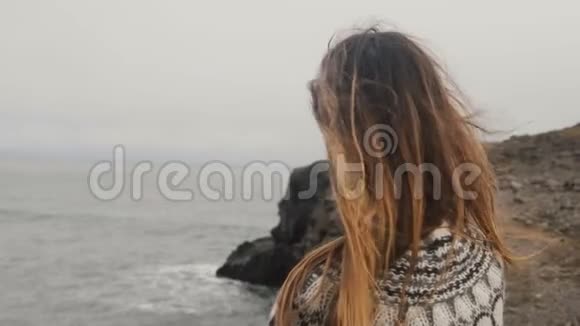 年轻幸福的女人站在海边看着镜头微笑着头发在风中飘扬视频的预览图