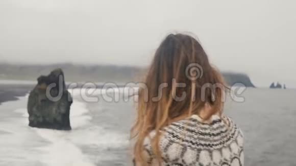 站在海边仰望冰岛巨魔脚趾的年轻黑发女子头发随风飘动视频的预览图