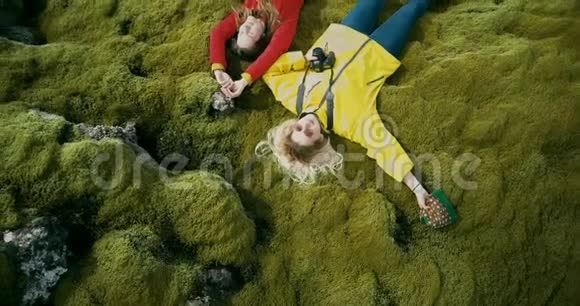 两个幸福的女人躺在冰岛熔岩场柔软的苔藓上的高空俯视旅游者依靠大自然视频的预览图