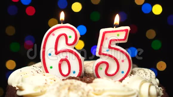 65号在蛋糕上面65岁生日蜡烛燃烧在最后吹灭彩色模糊背景视频的预览图