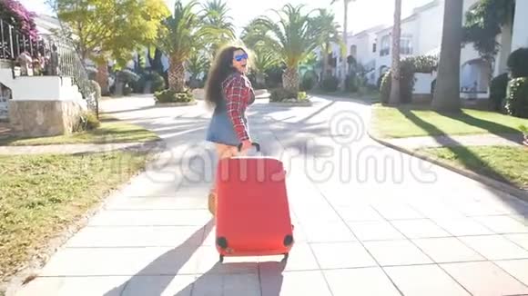 一个年轻的女人带着红色的手提箱跑在度假村里视频的预览图