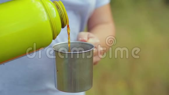 一个女人把热水瓶里的热茶倒进杯子里视频的预览图