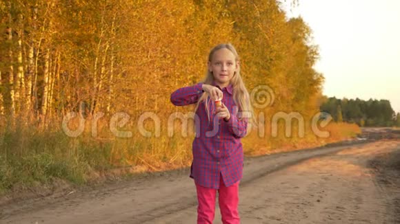 快乐的孩子在户外吹肥皂泡乡村路上的小女孩金色的秋天慢动作视频的预览图