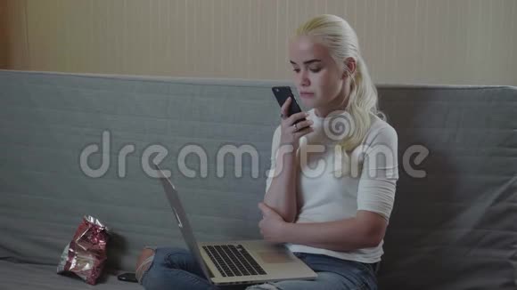 家中客厅的沙发上坐着一个暖色调的金发女郎用智能手机在线识别声音视频的预览图