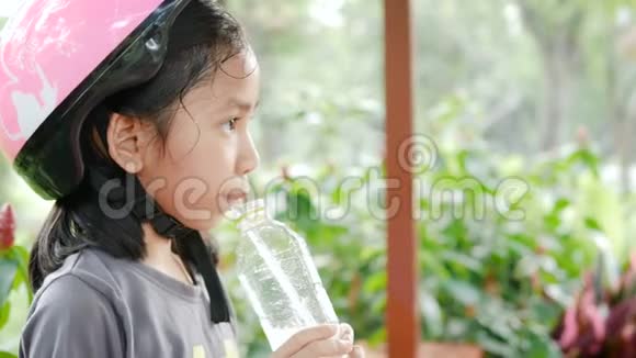 可爱的亚洲小女孩戴着粉红色的头盔在自然公园喝着幸福的水视频的预览图
