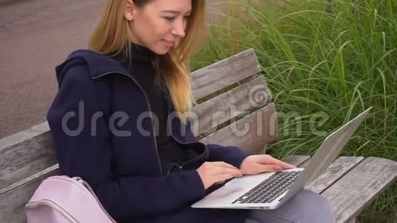 女性通过笔记本电脑在社交网络中聊天坐在草地附近的长凳上视频的预览图