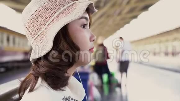 快乐的亚洲少女带着耳机听音乐在火车站等着夏天泰国旅游概念视频的预览图