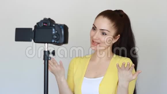 快乐微笑的女人或博主用手和说话的手势用固定在三脚架上的摄像机录制视频视频的预览图
