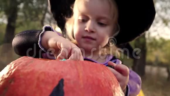 一个穿着女巫服装和帽子的小漂亮女孩从桶里拿出糖果秋天公园的万圣节视频的预览图