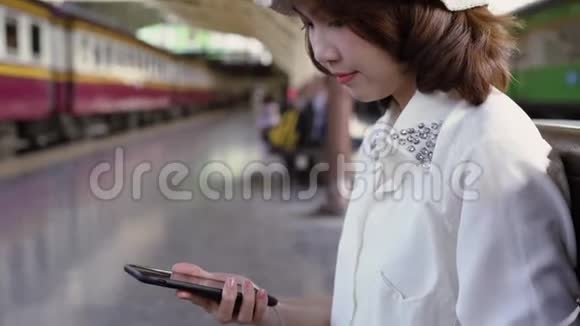 快乐的亚洲少女带着耳机听音乐在火车站等着夏天泰国旅游概念视频的预览图