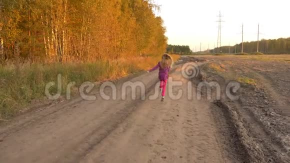 快乐的年轻女孩在田野附近的乡间小路上奔跑和跳跃秋天的金色黄昏小女孩视频的预览图