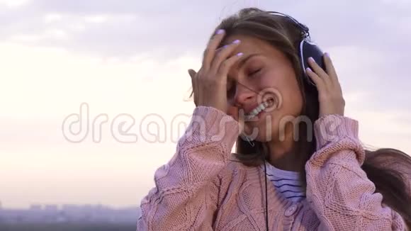 快乐的女孩听着音乐戴着耳机站在屋顶上视频的预览图