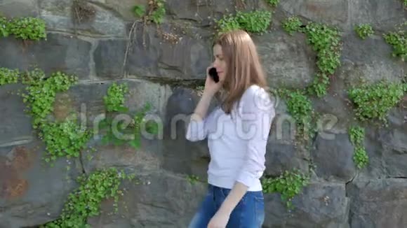 漂亮的年轻女孩走在古老的野石墙上在智能手机上交谈视频的预览图