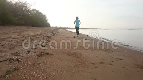 棕褐色的女孩跑在海滩上黎明时转身视频的预览图