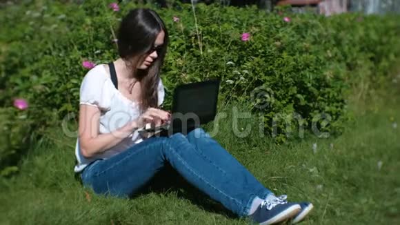 夏天美丽的黑发女孩坐在公园里用笔记本电脑打字视频的预览图