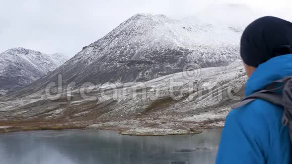 一个带背包的人在山里旅行他的周围是美丽的山脉和清澈的湖泊他拍了照片视频的预览图