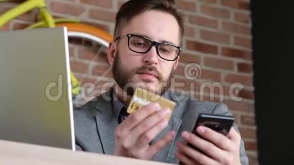 网上银行与智能手机一个留着胡子的时髦的现代年轻人用银行信用卡在视频的预览图