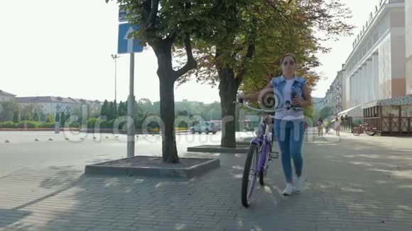 一个年轻快乐的女孩骑着自行车在城市里走来走去喝着咖啡的肖像视频的预览图