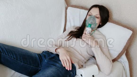 使用雾化器和吸入器进行治疗躺在沙发上的年轻女人通过吸入面罩吸入前景视频的预览图