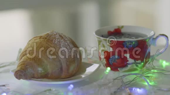 热气腾腾的茶与羊角面包装饰着闪烁的花环在桌子上视频的预览图
